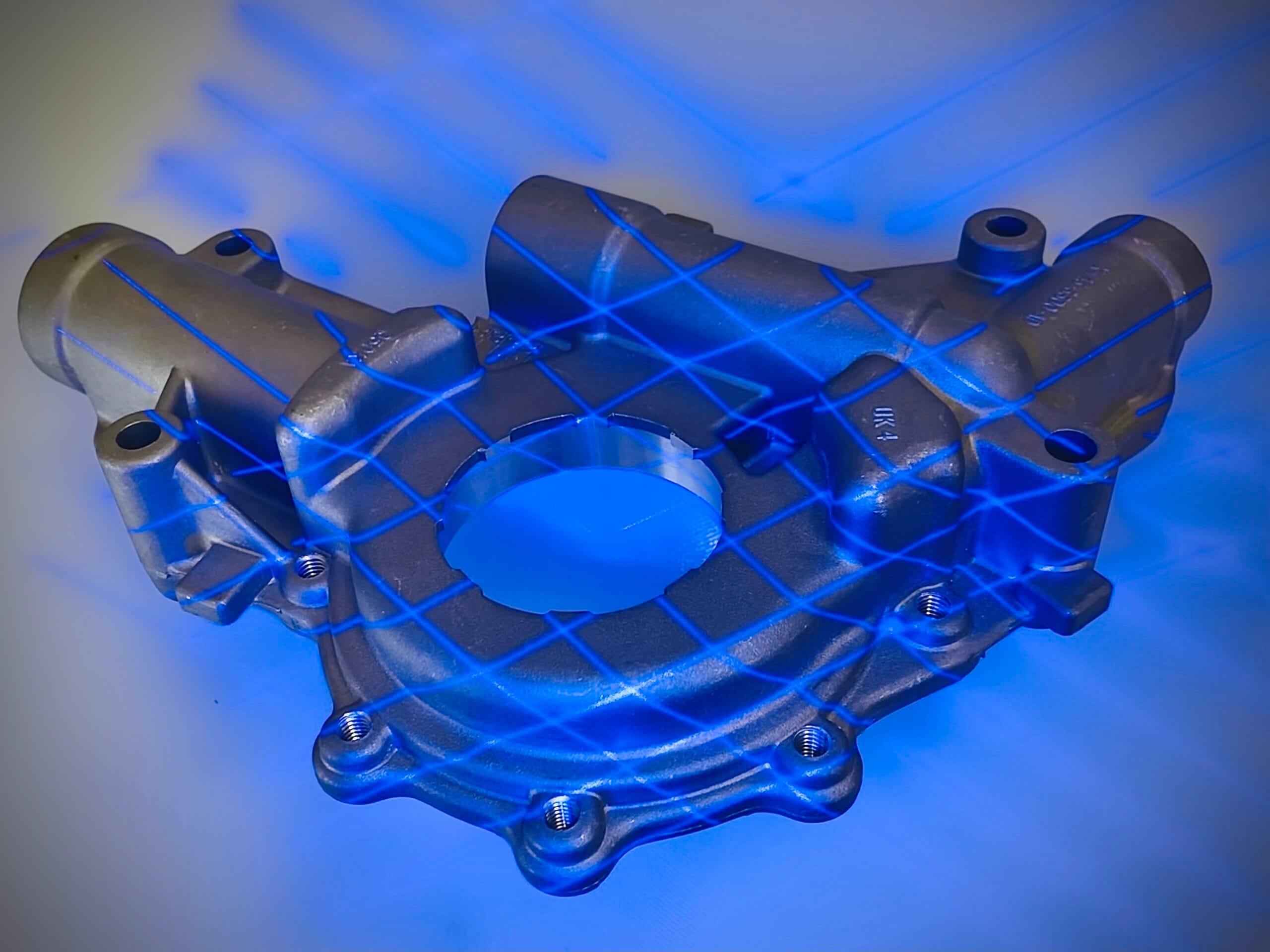 Silver automotive part with crossing blue laser lines over it during 3D scanning