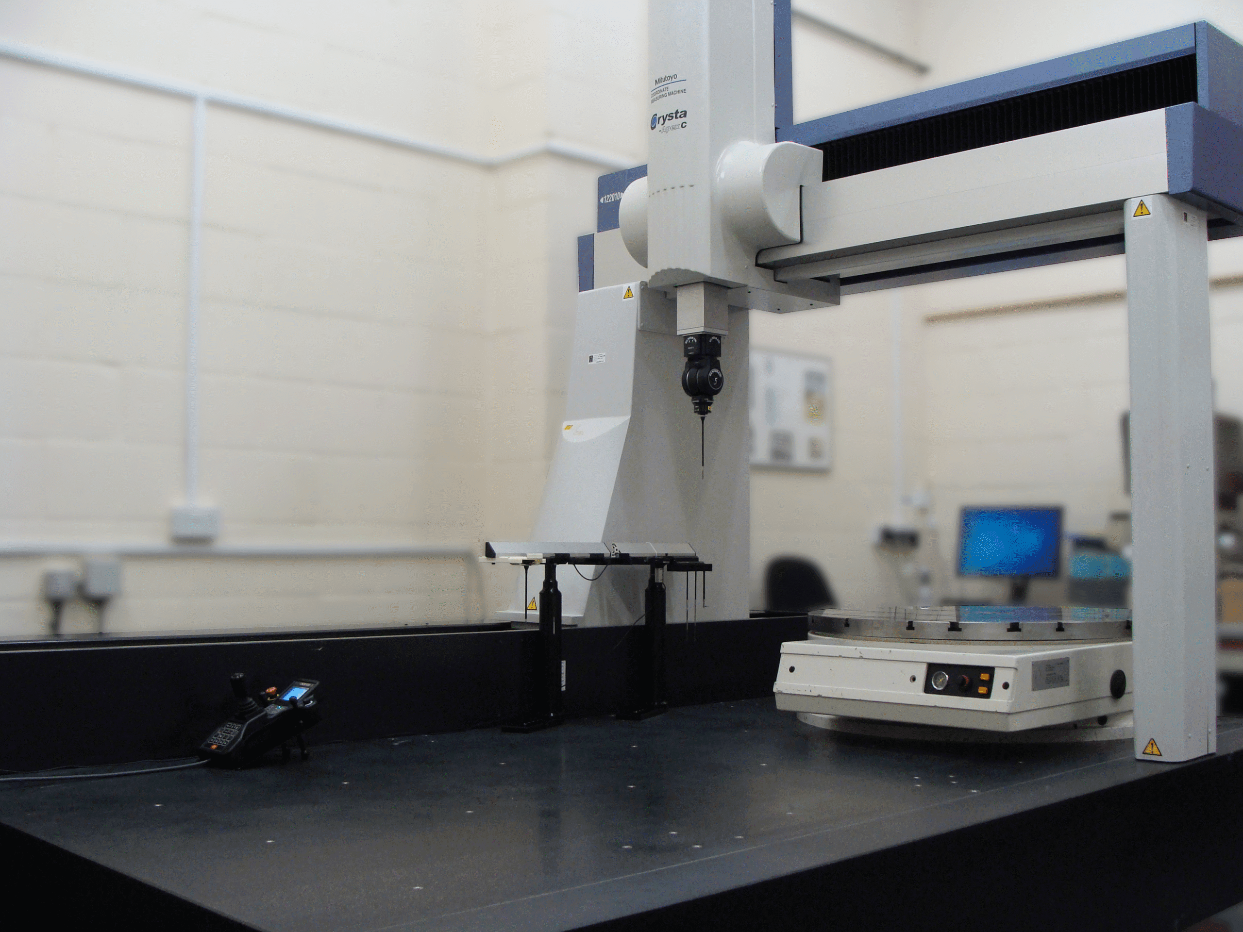 Photo of large CMM with white and blue bridge, black granite bed and black REVO probe head