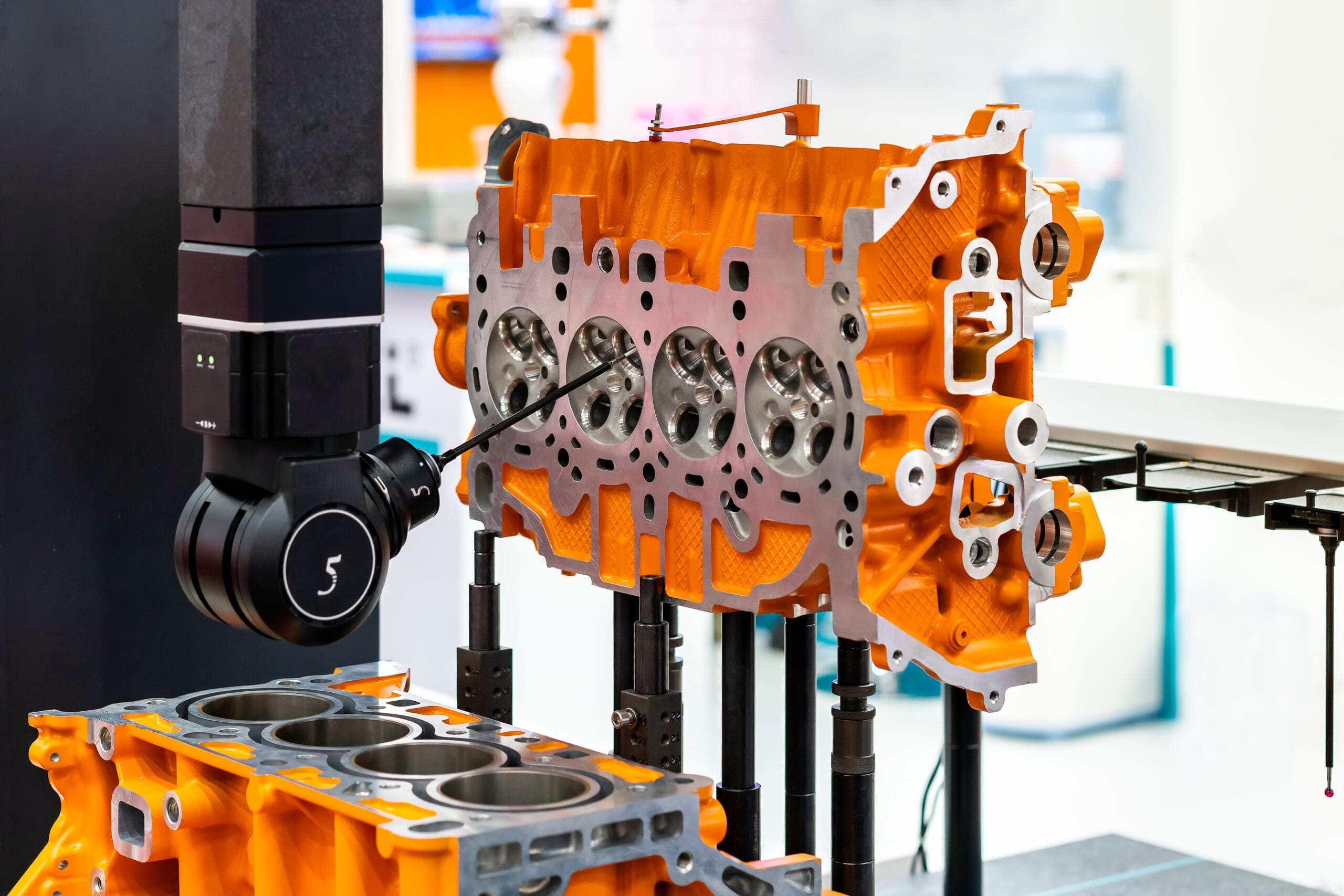Black REVO-2 CMM Probe head measuring bright orange engine block for CMM inspection